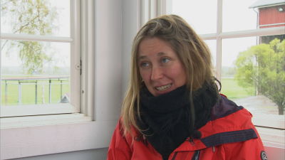 En kvinna med långt hår och röd jacka sitter intill ett fönster