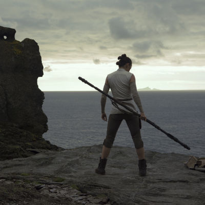 Rey (Daisy Ridley) tränar på en hög klippavsats vid havet.