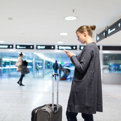 Kvinna på flygfält som petar på sin telefon. 