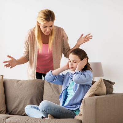 en mamma grälar med sin dotter som sitter på soffan och håller för öronen