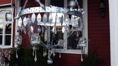 En hemgjord kristallkrona med stomme av spikband och kättingar, dekorerad med lila glaspärlor, klara kristaller och bladformade aluminiumbitar. Kristallkronan har ljushållare av återanvända glasburkar.