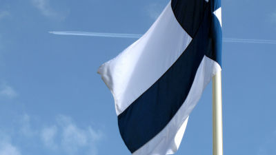 Flagga som snott sig en aning runt flaggstången. I bakgrunden ett flygplan.