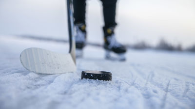 En puck och en ishockeyklubba på snöig isbana.
