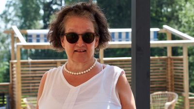 Monika Fagerholm står på en somrig terass och tittar in i kameran med solglasögon på.