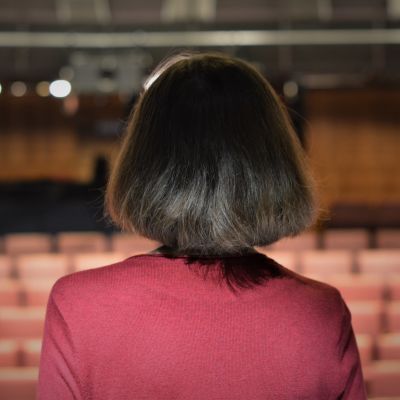 En kvinna i brun page och röd tröja ser ut över en tom teatersalong.