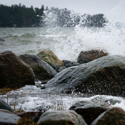 Havet stormar, vattnet slår mot klippor vid en strand.
