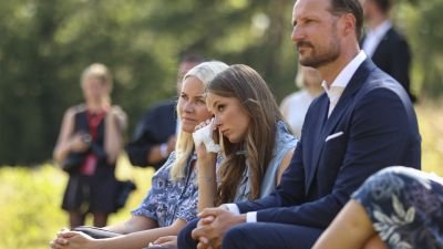 Konrprinsessan Mette-Marit, prinsessan Ingrid Alexandra och kronprins Haakon sitter på bänkar invid Utoyascenen. Ingrid Alexandra torkar bort en tår med en näsduk.