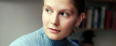 en kvinna i ljusblå tröja sitter framför en bokhylla och tittar till vänster