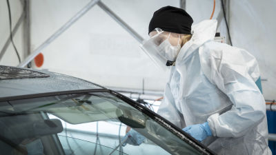 Suojavarusteisiin pukeutunut henkilö tekee koronatestiä autossa istuvalle henkilölle.