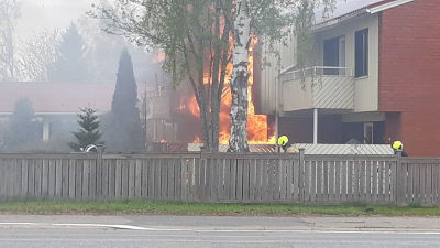 Rivitalo palaa, palomiehiä kävelee talon sivulla.