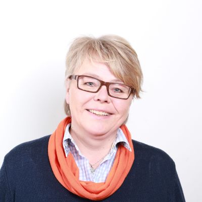 En glad kvinna med kort ljust hår och glasögon tittar in i kameran.