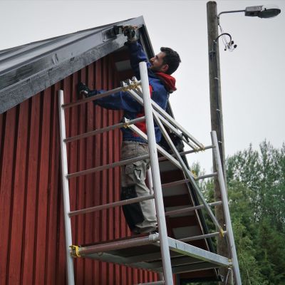 En man står på en byggställning och målar taket på ett hus.