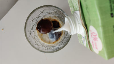 Någon häller mjölk i ett glas med frysta kaffekuber. Bilden är tagen uppifrån.