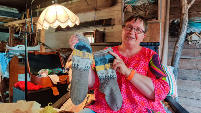 En kvinna sitter och håller upp två yllesockor.