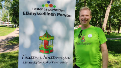 En man iklädd neongrön t-skjorta står bredvid ett högt plakat.