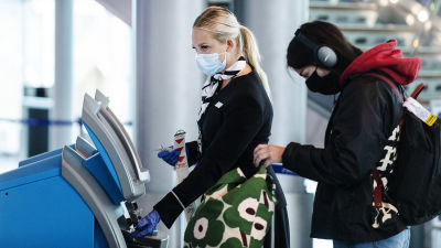 En Finnair-flygvärdinna i munskydd på Helsingfors-Vanda flygplats. Bakom henne en annan resenär i munskydd.