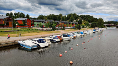 Båtar som gubbar i en å på rad intill en stenmur.