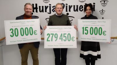 Tre personer håller upp skyltar med siffror som visar hur mycket understöd som en sparbanksstiftelse delat ut.