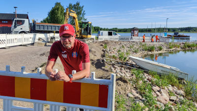 En man lutar över ett byggstaket på en arbetsplats nere vid en strand.