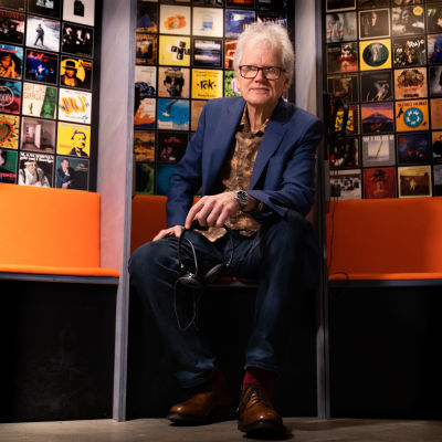 Tapio Korjus istuu penkillä Rockadillo - 50 vuotta kaikkiin suuntiin -näyttelyssä.