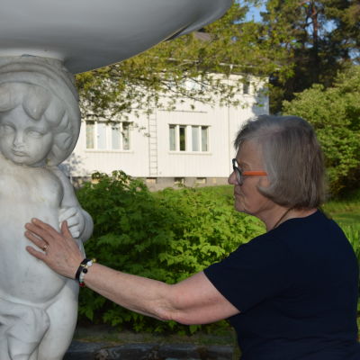 En äldre kvinna känner på en skulptur i vit marmor.