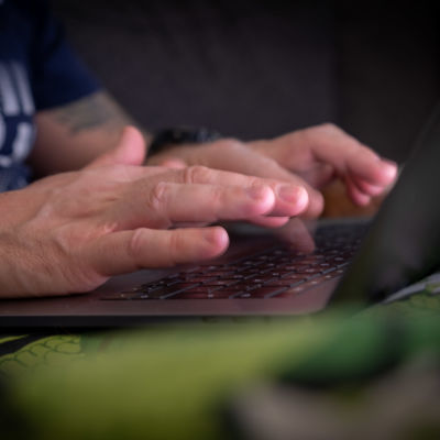 Lähikuva: mies kirjoittaa kannettavalla tietokoneella.