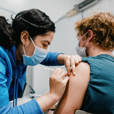 En sjukskötare i munskydd vaccinerar en person som också bär munskydd.