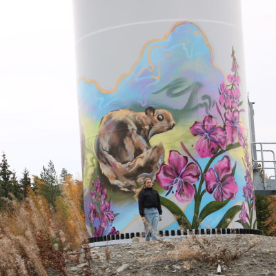 En kvinna med mörk jacka står framför en väggmålning på ett vindkraftverk.