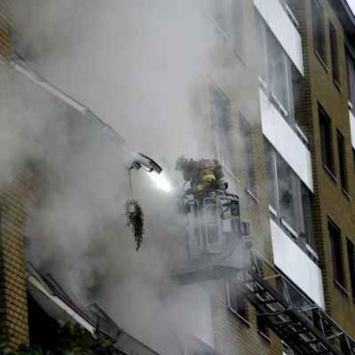 Brandman i skylift spanar in i ett brinnande hus.
