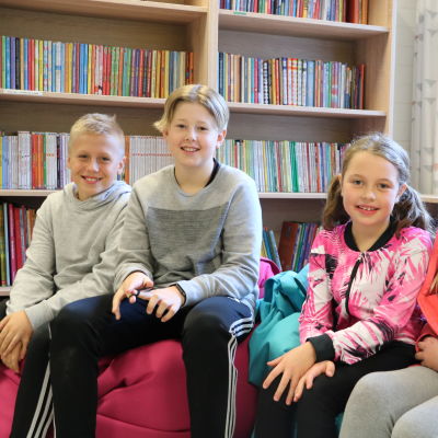 Fyra lågstadieelever, två pojkar till vänster och två flickor till höger sitter framför en bokhylla.
