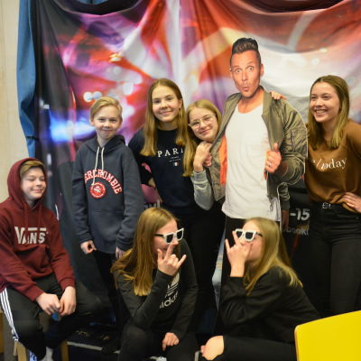 En grupp elever står bredvid pappfiguren Jontti Granbacka som leder MGP-showen i tv.