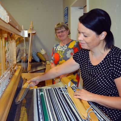 Näppi-opettaja Raija Nikkola (vas.) toivoo kangaspuista ehkä seuraavaa käsityöhittiä. Satu Seppälä kutoo jo trendiksi tullutta räsymattotyynyä.