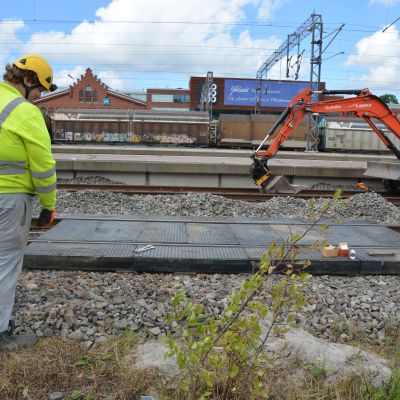 Två byggnadsarbetare står med ryggen vända vid ett brobygge över järnvägsspår. 