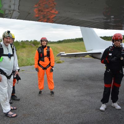 Fyra personer iklädda fallskärmshoppningsutrustning står bredvid ett flygplan.