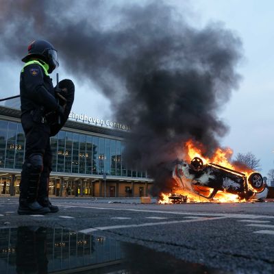 Två kravallutrustade poliser står bredvid en brinnande bil