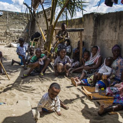 ryhmä ihmisiä istuu muurin varjossa Mosambikissä, etualalla pieni lapsi
