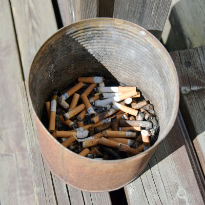 Rostig plåthink med cigarettfimpar utomhus.