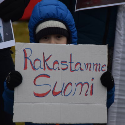 Ett asylsökande barn visar upp en skylt med texten "Rakastamme Suomi".