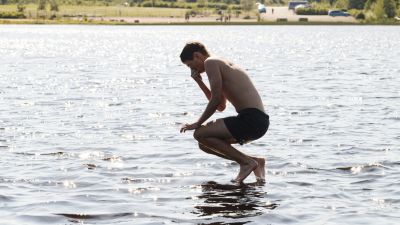 En pojke hoppar i vattnet vid en badstrand.