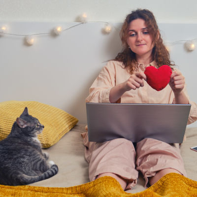 Kvinna sitter på en säng med sin katt och håller i ett tyghjärta. 