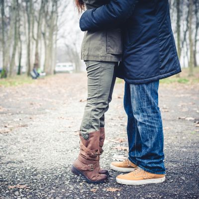 Benen på en man och en kvinna står mot varann ute i en park och kysser varann
