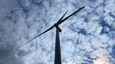 en bild av en vindmölla taget från marken så man ser rotorbladen och den molniga himlen