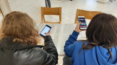 Två flickor sitter vid lunch med sina mobiltelefoner.