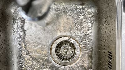 Vatten rinner från en kran ned i en diskho av stål.