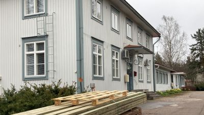 Ett gråblått trähus med en brädhög i förgrunden.