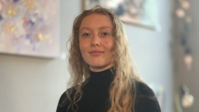 En ung kvinna med långt lockigt blont hår ser rakt in i kameran