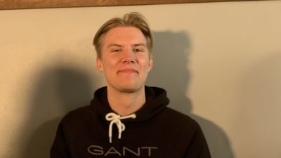 En ung man med ljust hår och mittbena tittar in i kameran.