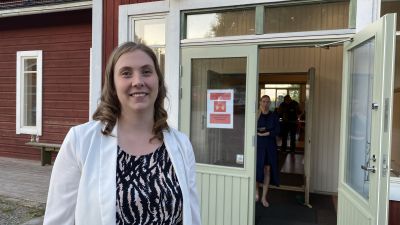 En kvinna står utanför ett rött trähus.