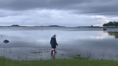 En kvinna med regnrock och gummistövlar vadar vid en havsstrand.