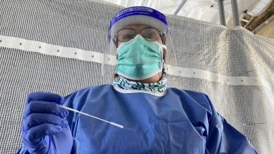 En skötare klädd i skyddsutrustning står framför kameran, redo att utföra ett coronatest.